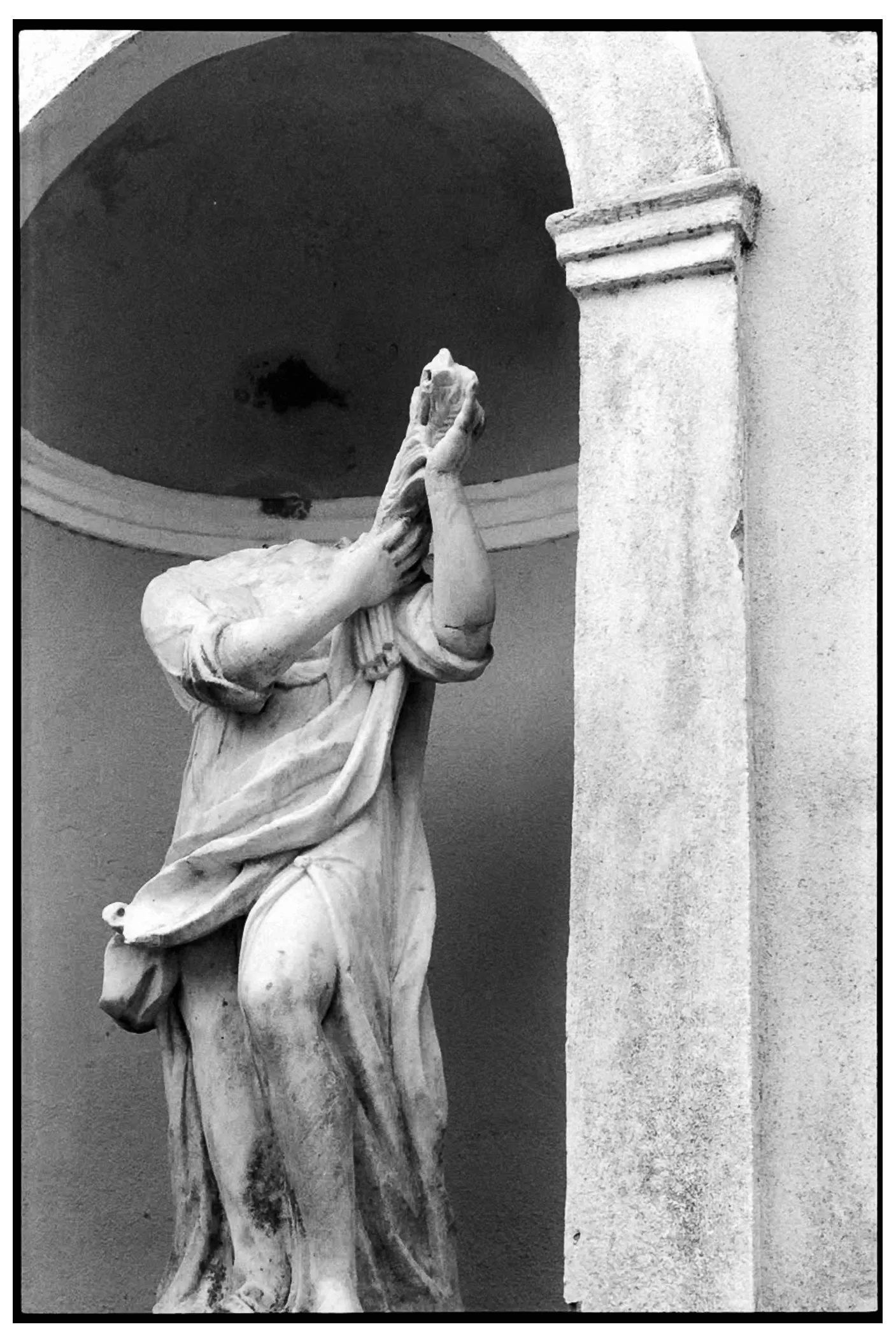 Headless classical statue in a wall niche, arms raised